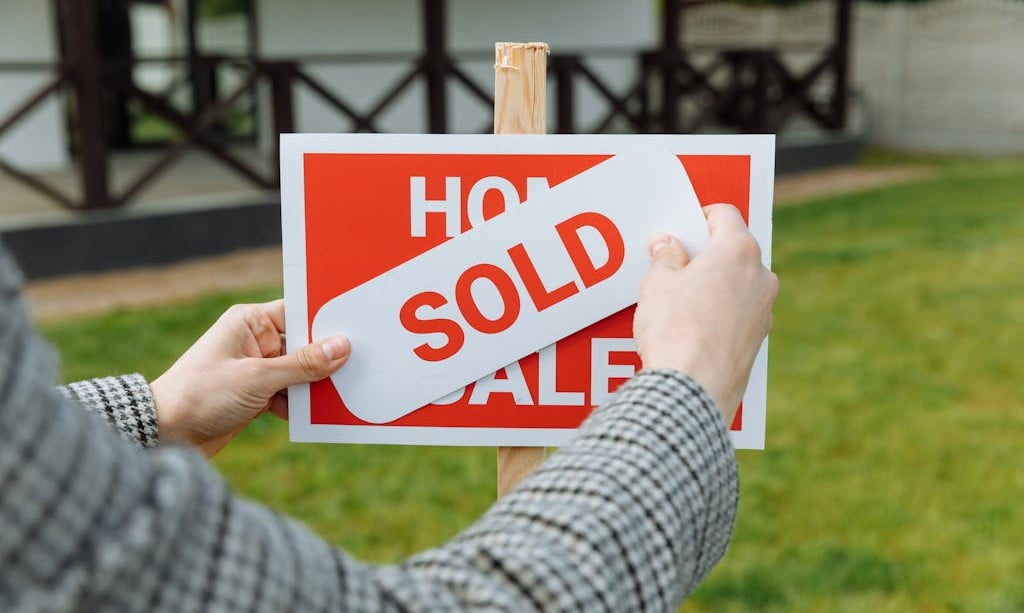 View of realtor's hands placing a "SOLD" sticker over a sign that reads "Home for sale".